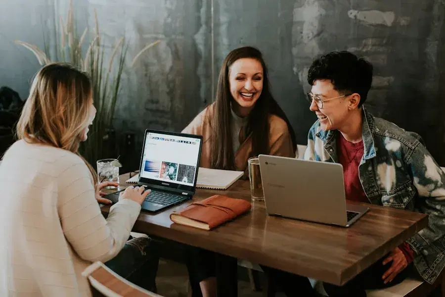 Three friends laughing over laptops at a café table
