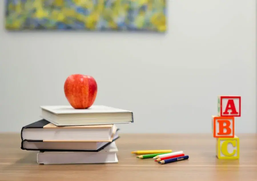 An apple on a stack of books beside ABC blocks and crayons